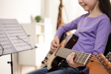 Photo of Little girl playing guitar at music lesson, closeup. Learning notes