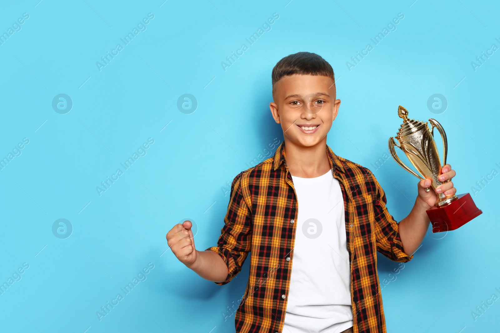 Photo of Happy boy with golden winning cup on blue background