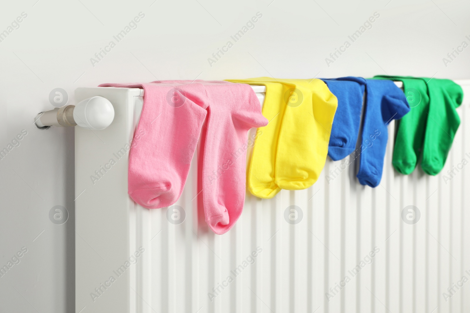 Photo of Different colorful socks hanging on white radiator indoors