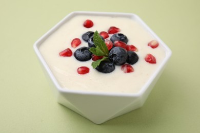 Photo of Bowl of delicious semolina pudding with blueberries, pomegranate and mint on light green background, closeup