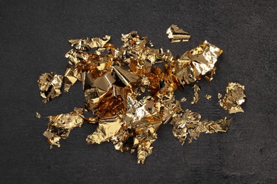 Photo of Many pieces of edible gold leaf on textured table, flat lay