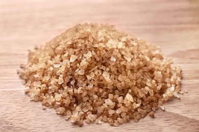 Photo of Pile of brown sea salt on wooden table, closeup. Spa treatment