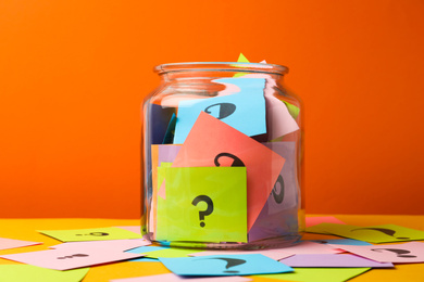 Photo of Colorful cards with question marks in glass jar on orange background