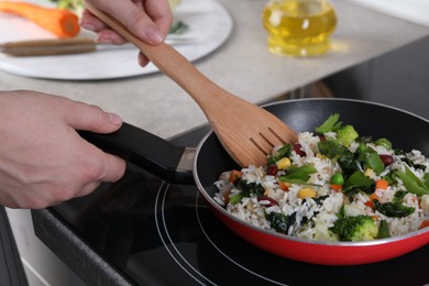 Photo of Woman frying rice with vegetables at induction stove, closeup