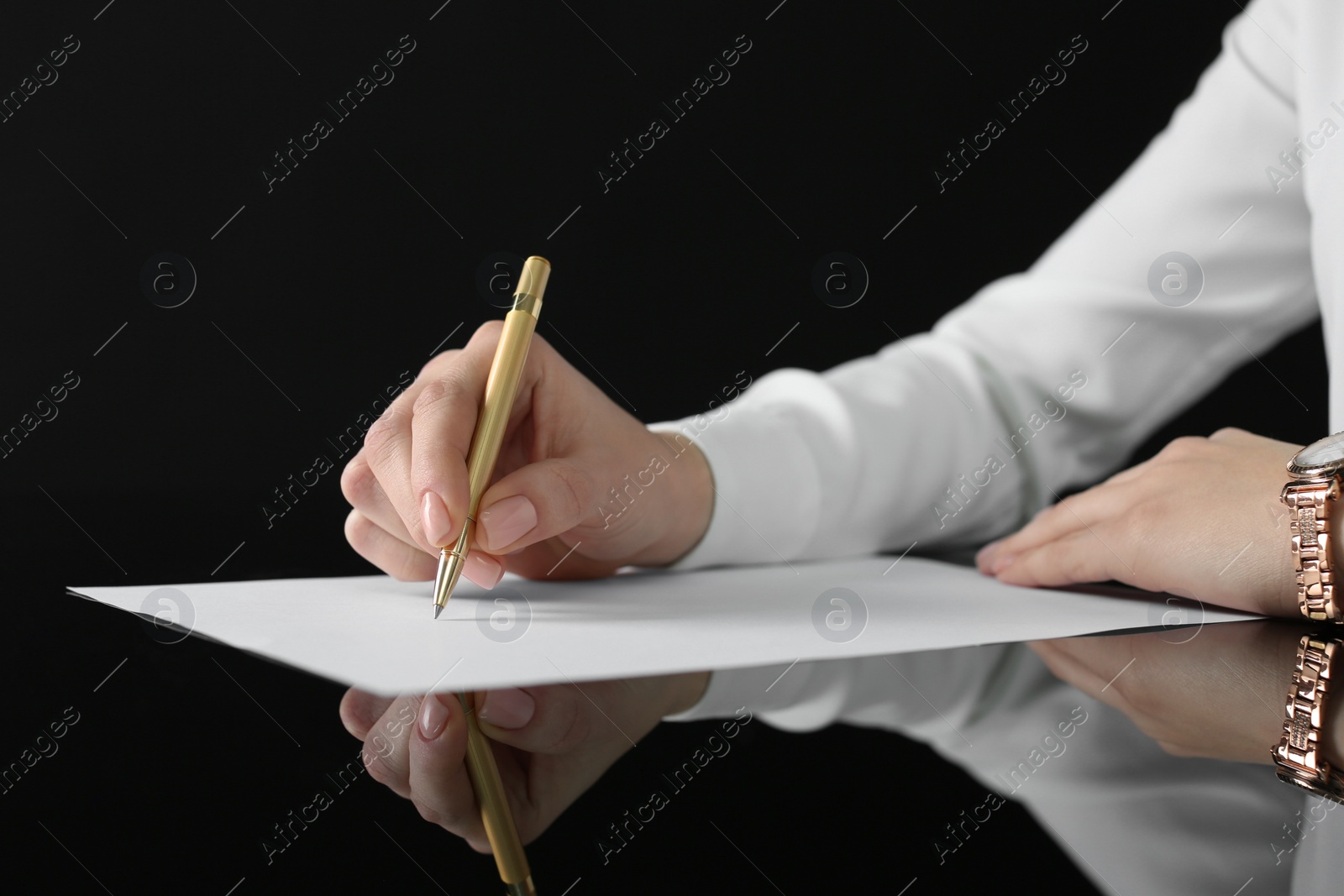 Photo of Woman writing on sheet of paper at glass table, closeup