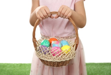 Photo of Little girl with basket full of Easter eggs on green grass against white background, closeup