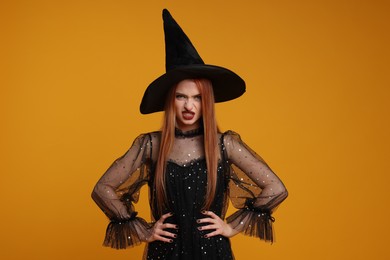 Young woman in scary witch costume on orange background. Halloween celebration