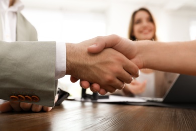 Business partners shaking hands at table after meeting in office, closeup