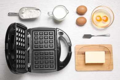 Photo of Flat lay composition with ingredients and Belgian waffle maker on white wooden table