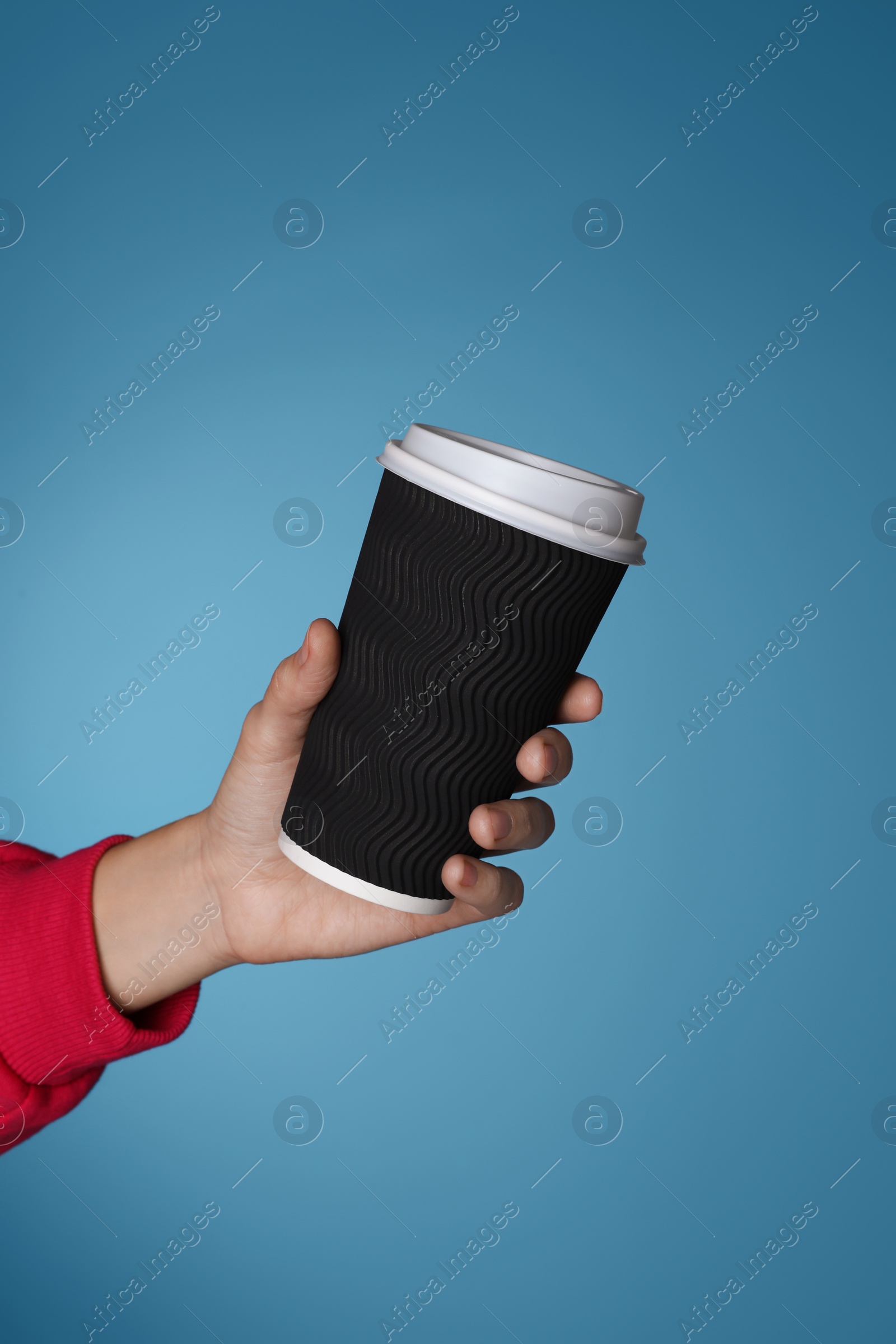 Photo of Woman holding takeaway paper coffee cup on blue background, closeup