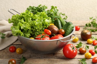 Wet vegetables in colander on wooden table, closeup