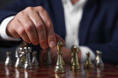 Photo of Man moving chess piece on checkerboard against dark background, closeup