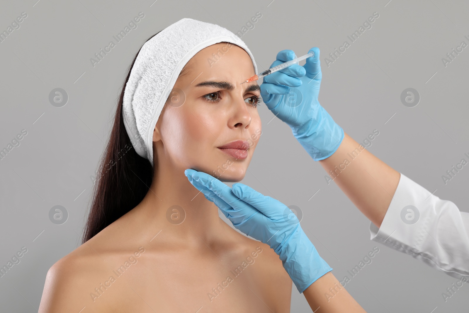 Photo of Doctor giving facial injection to young woman on light grey background. Cosmetic surgery