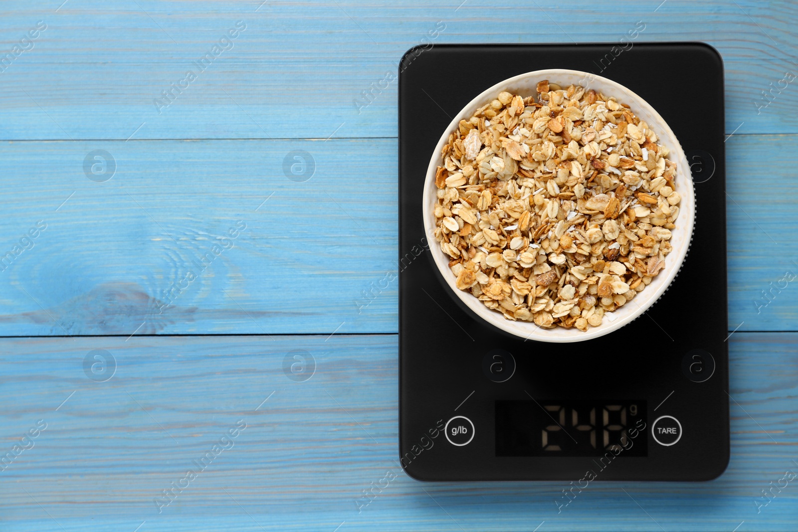 Photo of Digital kitchen scale with muesli on light blue wooden table, top view. Space for text