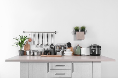 Set of clean cookware, dishes, utensils and appliances on table at white wall