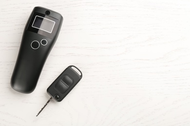 Photo of Modern breathalyzer and car key on white wooden table, flat lay. Space for text