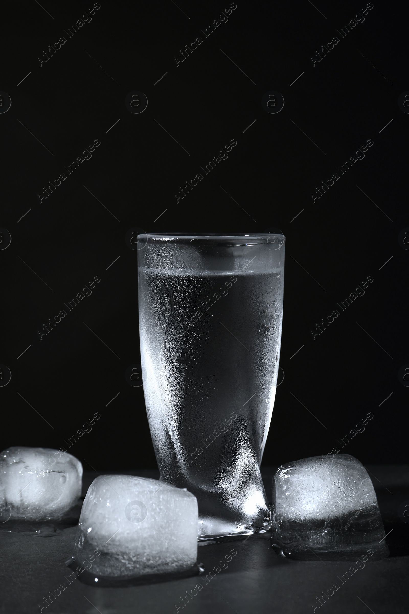 Photo of Vodka in shot glass with ice on table against black background