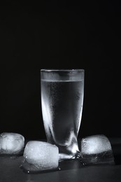 Vodka in shot glass with ice on table against black background