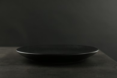 Beautiful ceramic plate on gray table against black background, closeup. Space for text