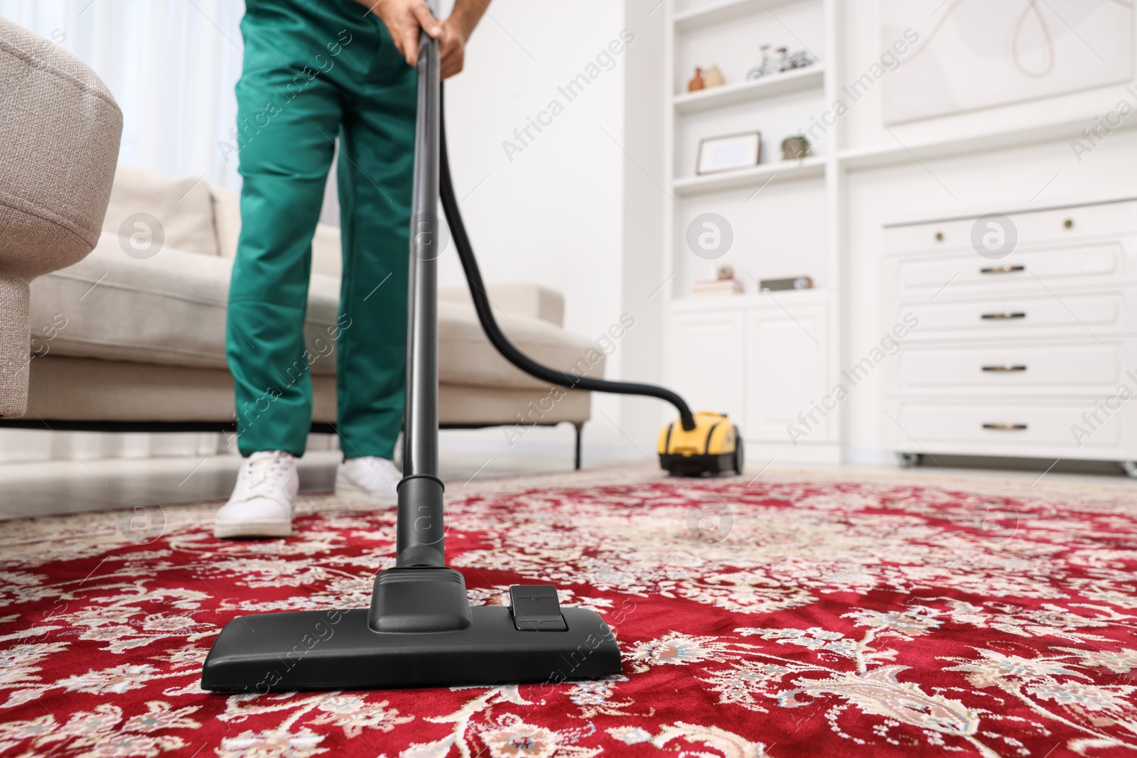 Photo of Dry cleaner's employee hoovering carpet with vacuum cleaner indoors, closeup. Space for text