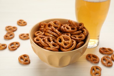Photo of Delicious pretzel crackers and glass of beer on white wooden table, closeup