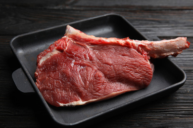 Photo of Fresh raw beef cut in baking dish on wooden table, closeup
