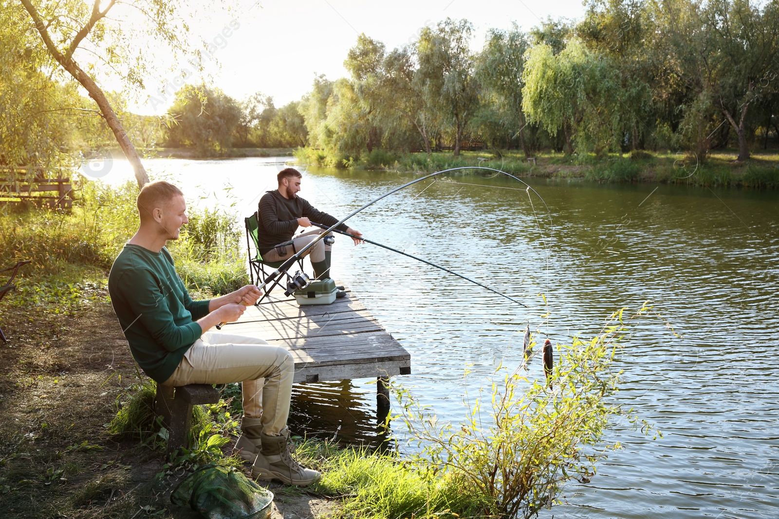 Photo of Friends fishing on wooden pier at riverside. Recreational activity