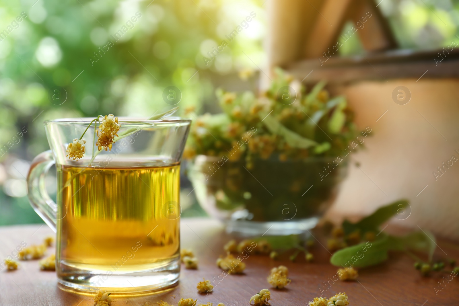 Photo of Glass cup of aromatic tea with linden blossoms on wooden table against blurred background, space for text