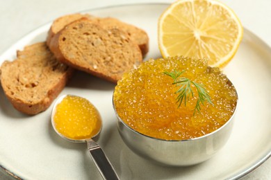 Photo of Fresh pike caviar in bowl, lemon and bread on light table, closeup