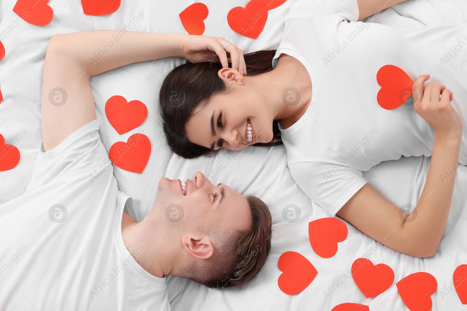 Photo of Lovely couple on bed with many decorative hearts, top view. Valentine's day celebration