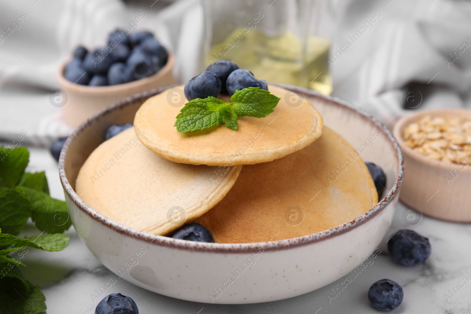 Photo of Bowl with tasty oatmeal pancakes, mint and blueberries on table, closeup