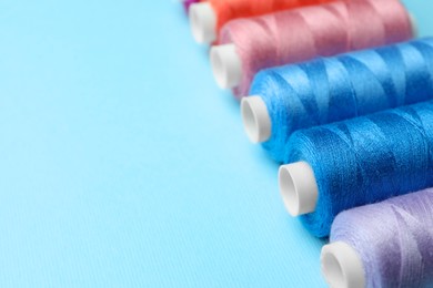 Photo of Set of different colorful sewing threads on light blue background, closeup. Space for text