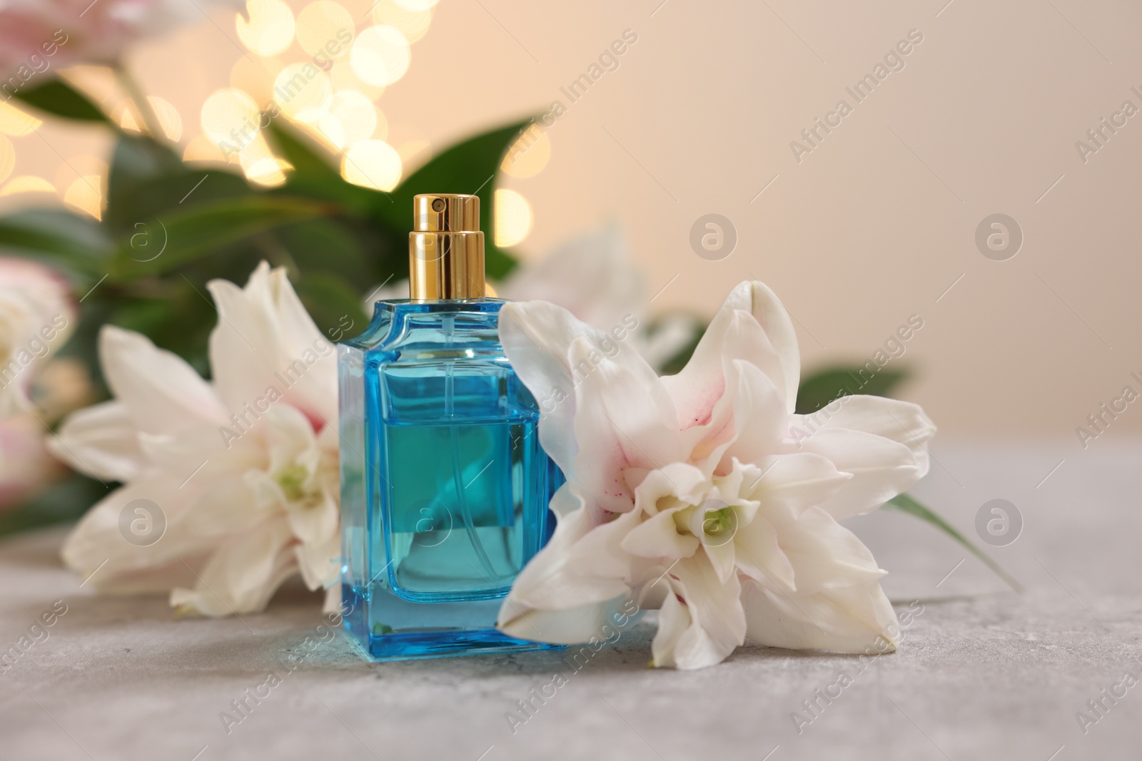 Photo of Bottle of perfume and beautiful lily flowers on table against beige background with blurred lights, closeup