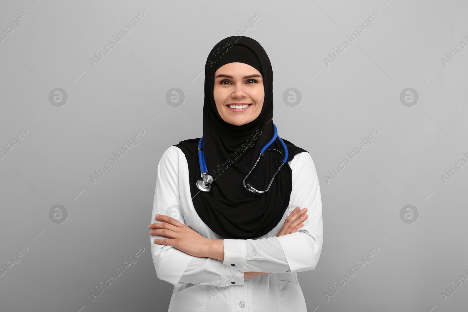 Photo of Muslim woman wearing hijab, medical uniform with stethoscope on light gray background