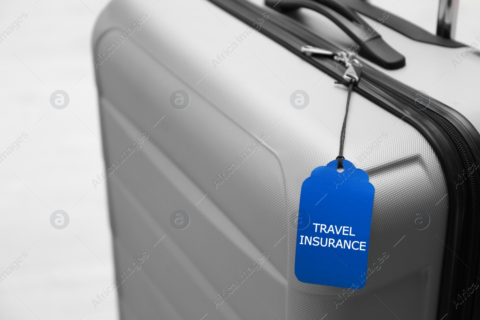 Photo of Grey suitcase with TRAVEL INSURANCE label on blurred background, closeup