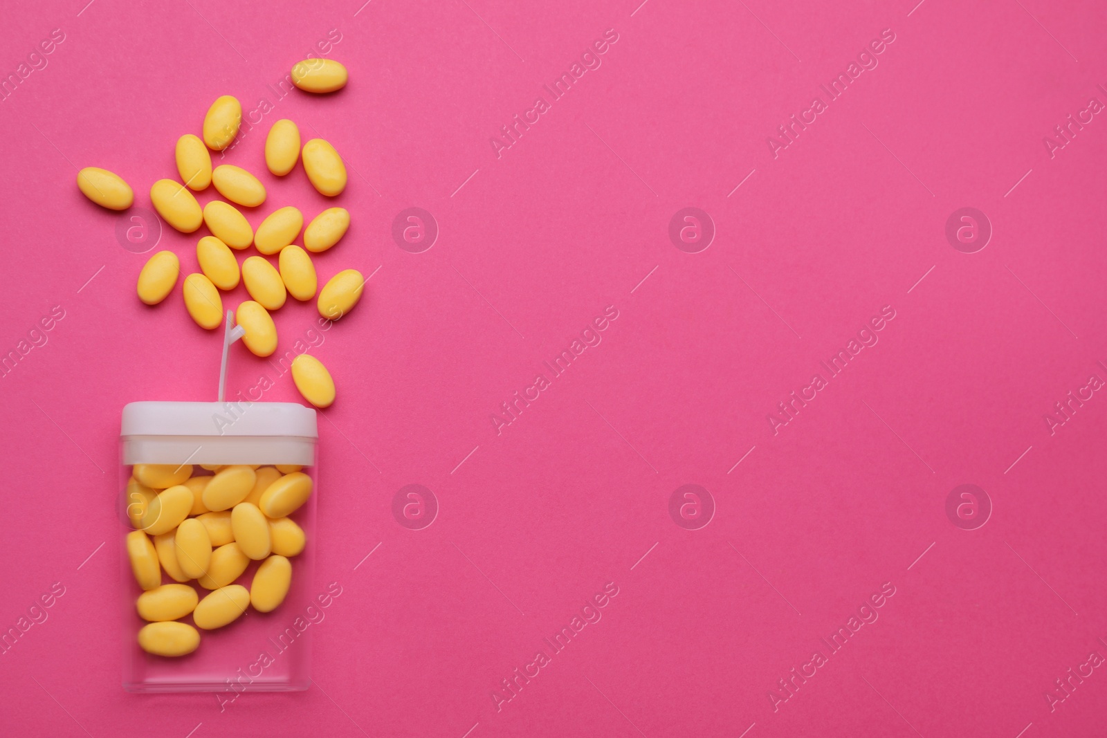 Photo of Tasty yellow dragee candies and container on pink background, flat lay. Space for text
