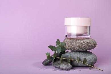 Photo of Jar of body cream with eucalyptus and stacked stones on lilac background. Space for text