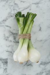 Photo of Bunch of green spring onions on white marble table, flat lay