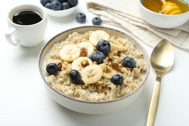 Photo of Tasty oatmeal with banana, blueberries, walnuts and honey served in bowl on white wooden table