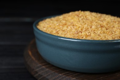 Photo of Bowl of uncooked bulgur on black wooden table, closeup