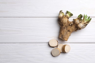 Photo of Cut horseradish root on white wooden table, flat lay. Space for text