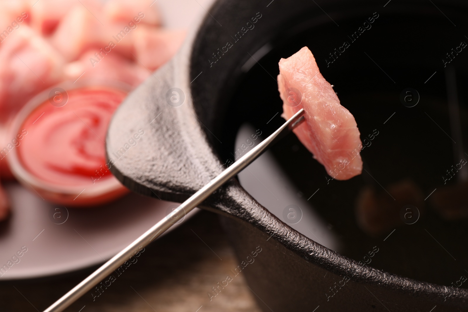 Photo of Fondue pot and fork with piece of raw meat on wooden table, closeup