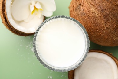 Photo of Glass of delicious vegan milk, coconuts and flower on green background, flat lay