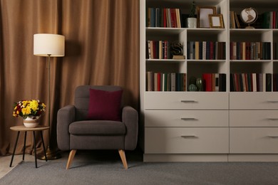 Cozy home library interior with comfortable armchair, floor lamp and collection of books on shelves