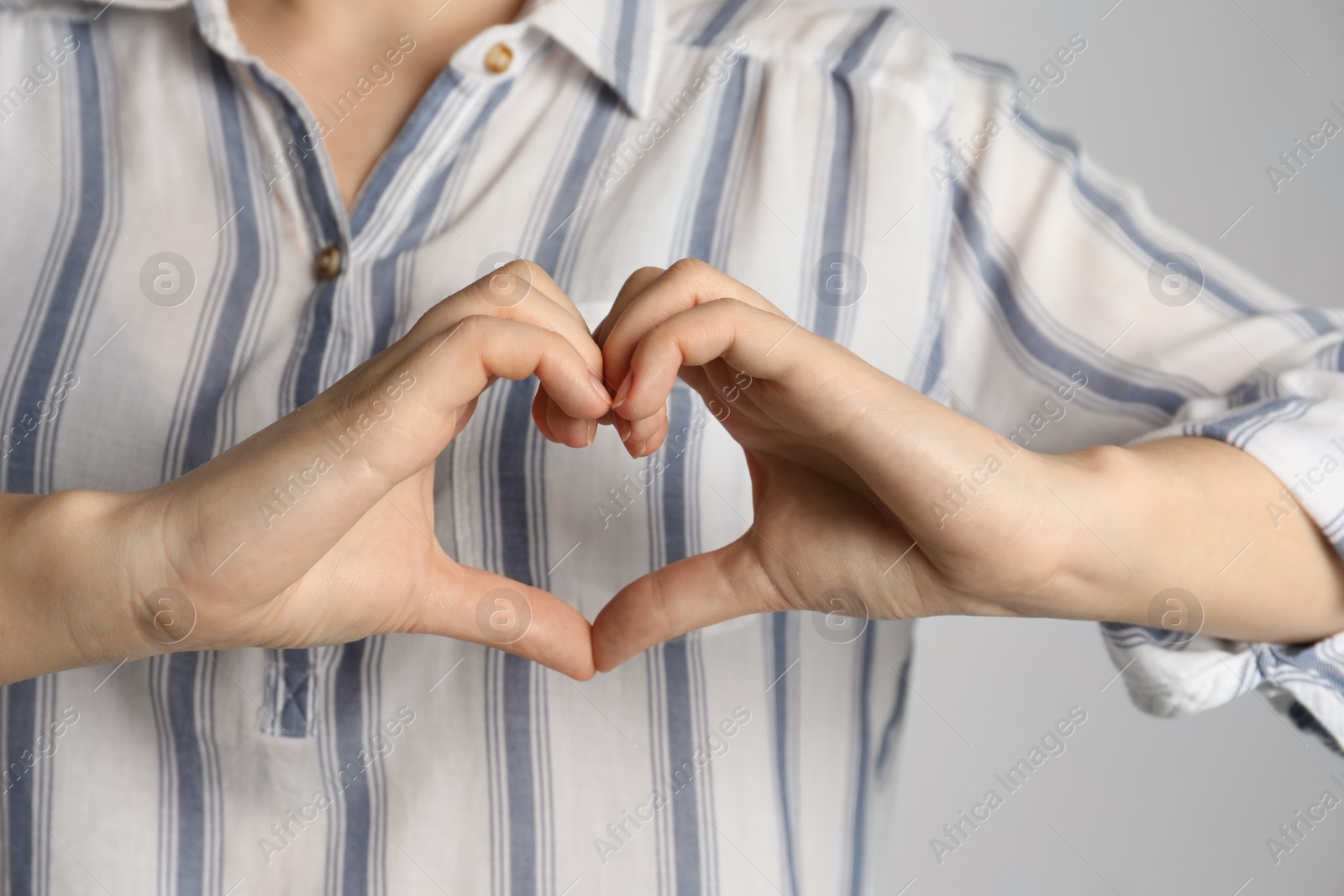 Photo of Woman making heart with her hands on light grey background, closeup