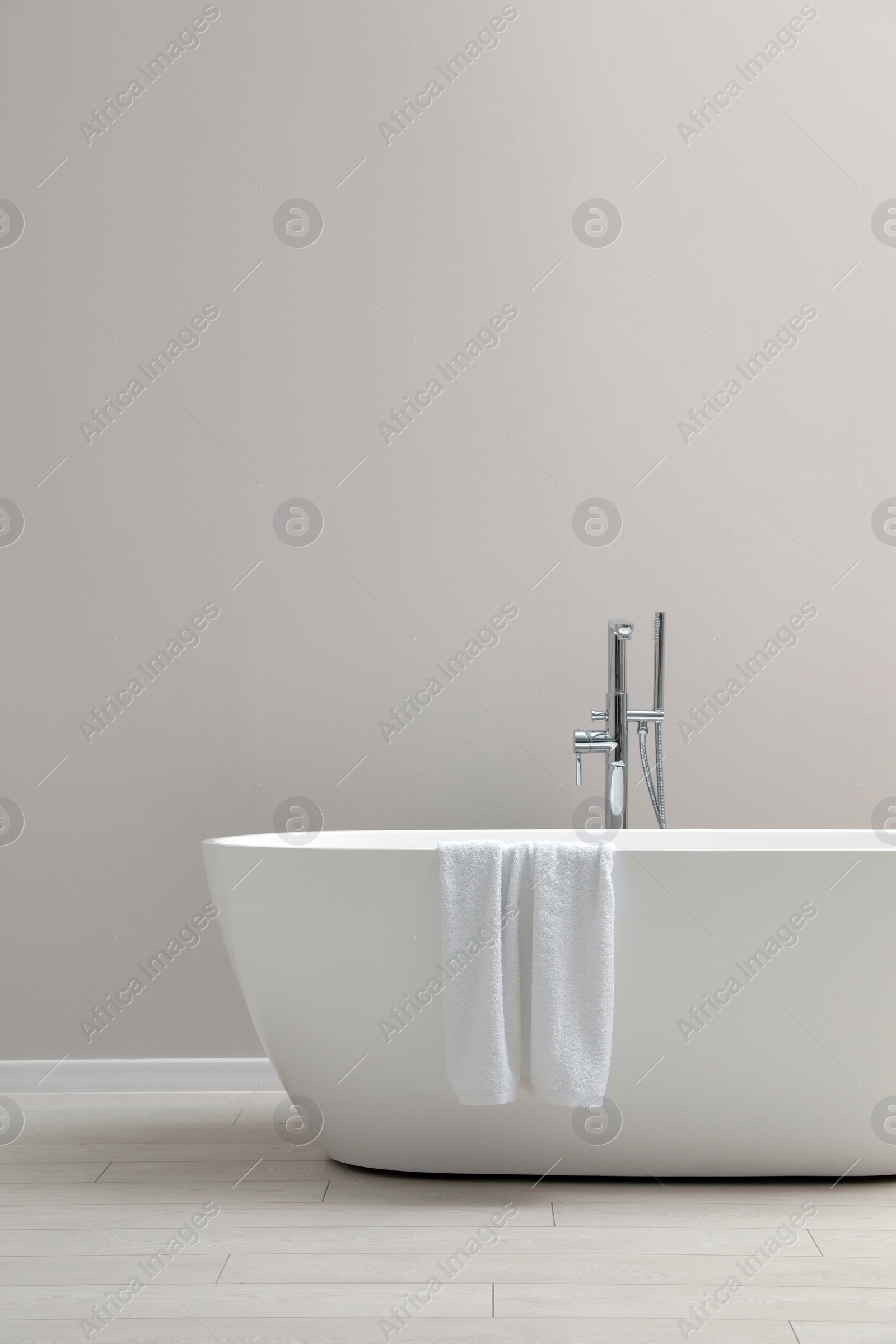 Photo of Modern ceramic bathtub with towel near light wall indoors