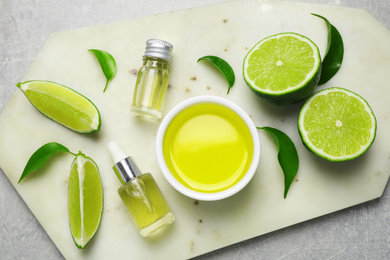 Lime essential oil and cut citrus fruits on light grey table, top view