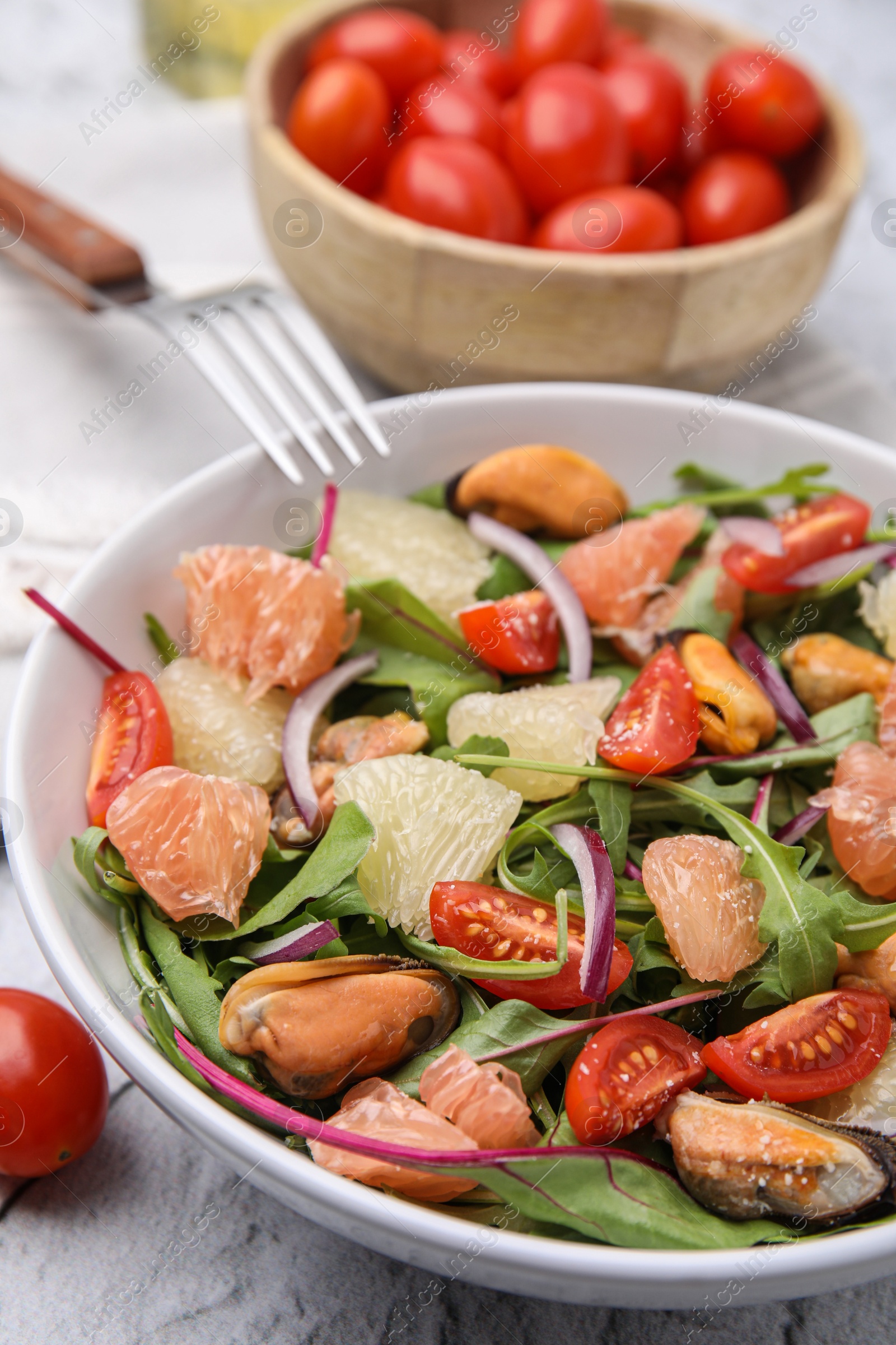 Photo of Delicious pomelo salad with tomatoes and mussels on white textured table, closeup