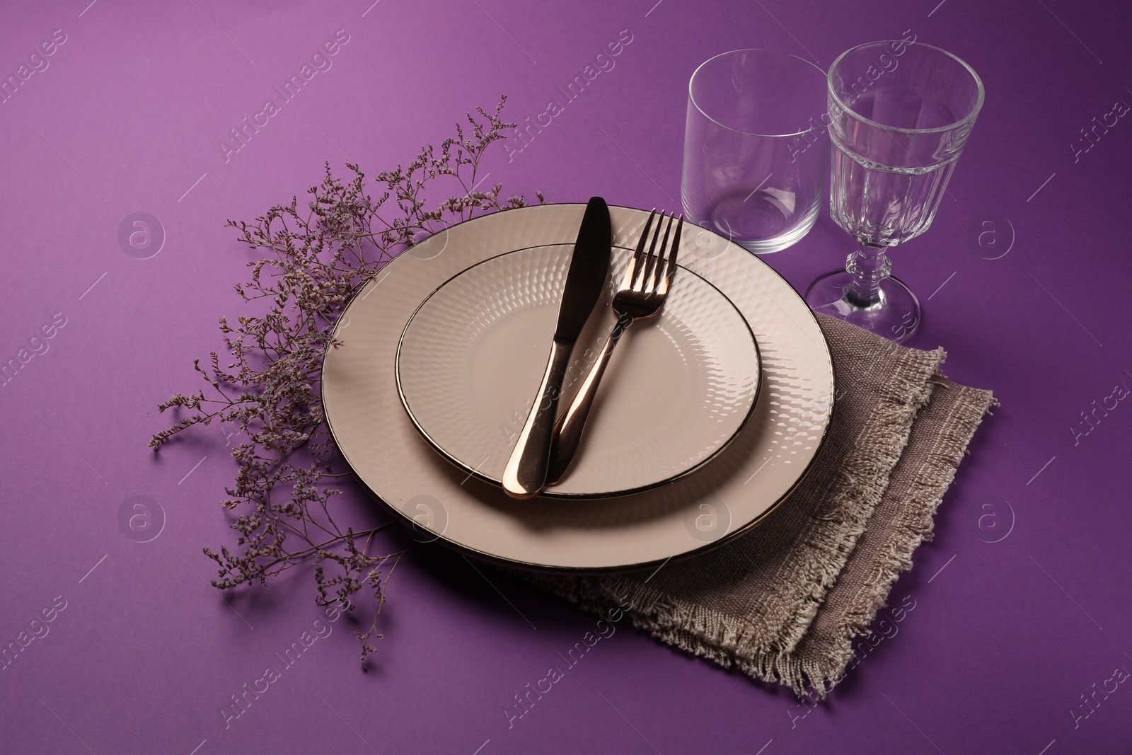 Photo of Stylish table setting. Plates, cutlery, glasses and floral decor on purple background