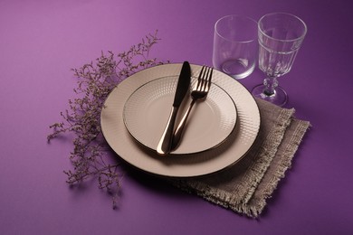 Photo of Stylish table setting. Plates, cutlery, glasses and floral decor on purple background